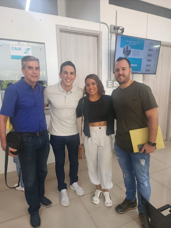 Cuatro personas posando en una oficina con módulo de caja y pantalla de turnos